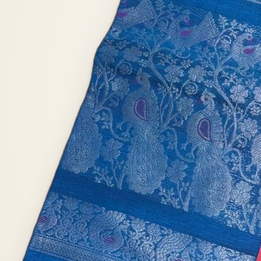 Close view of a peacock-blue pallu with woven peacocks and vines, beside a coral-red body.
