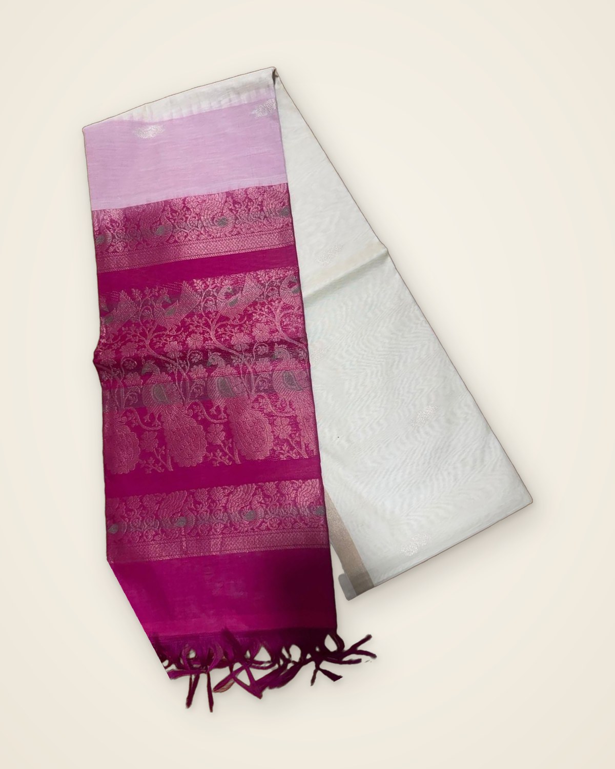 Ivory saree with a magenta pallu and pale pink band, woven with peacocks and paisleys, folded on a plain ivory backdrop.